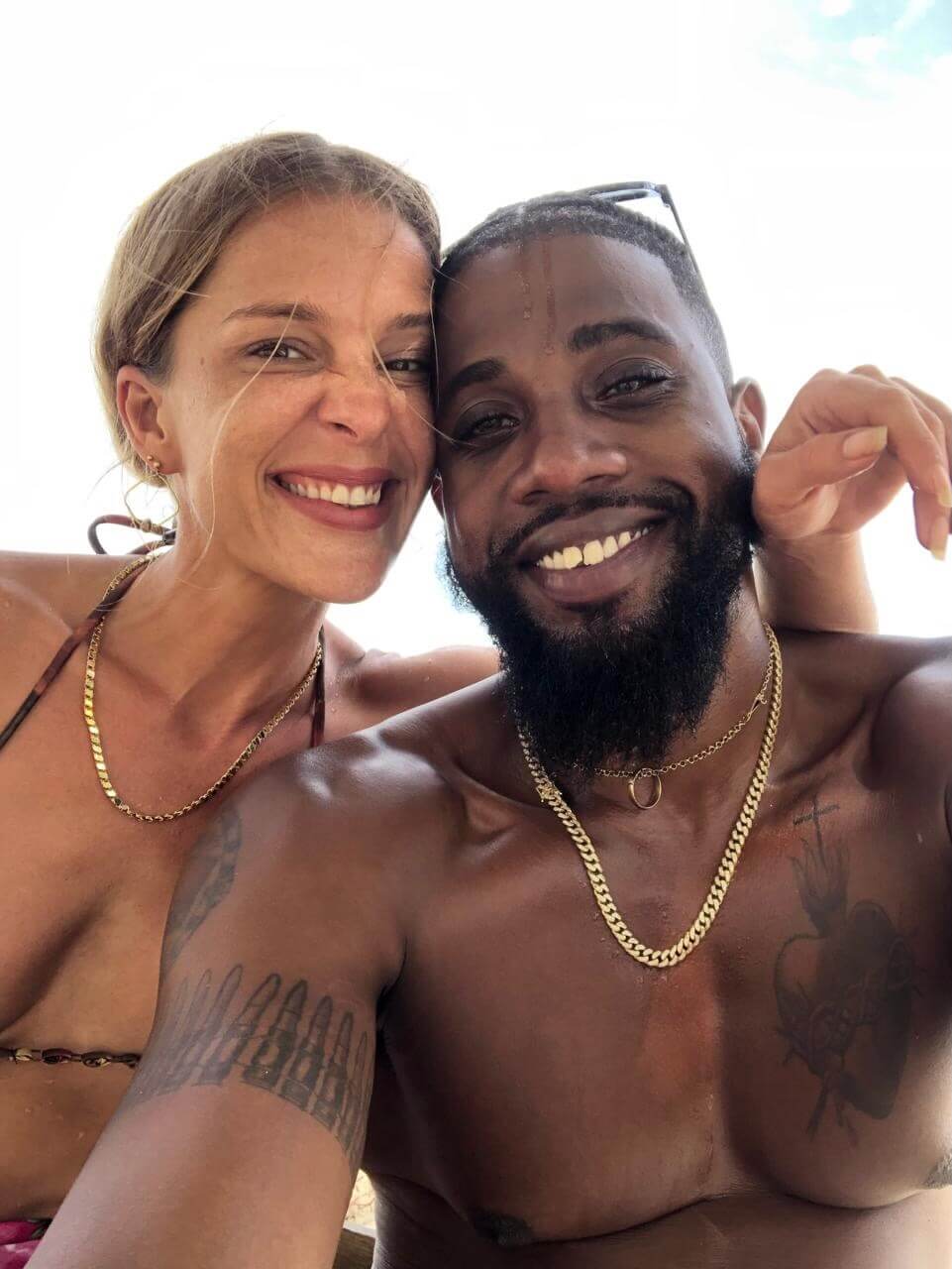 blonde German woman hugs dark Trinidadian male dripping sea water on Tobago beach